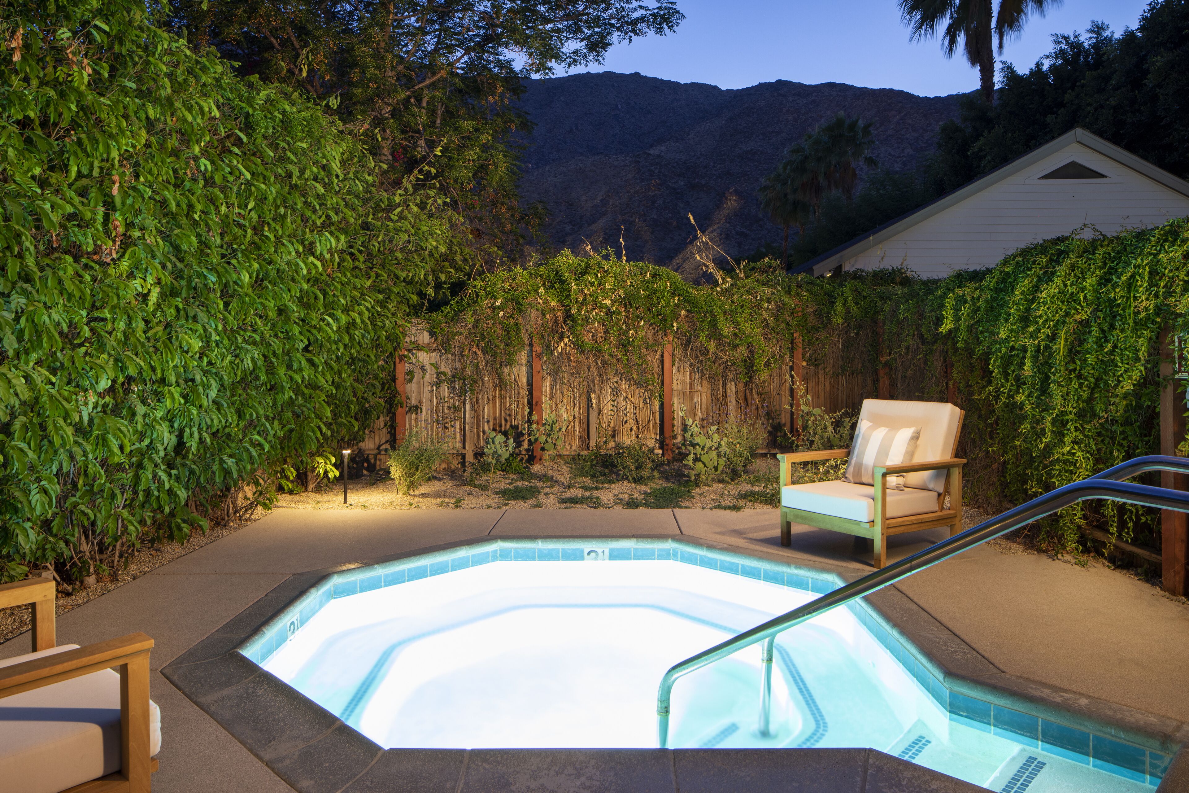 Una piscina con cubierta de madera y una silla, rodeada de exuberante vegetación y un telón de fondo de montañas.