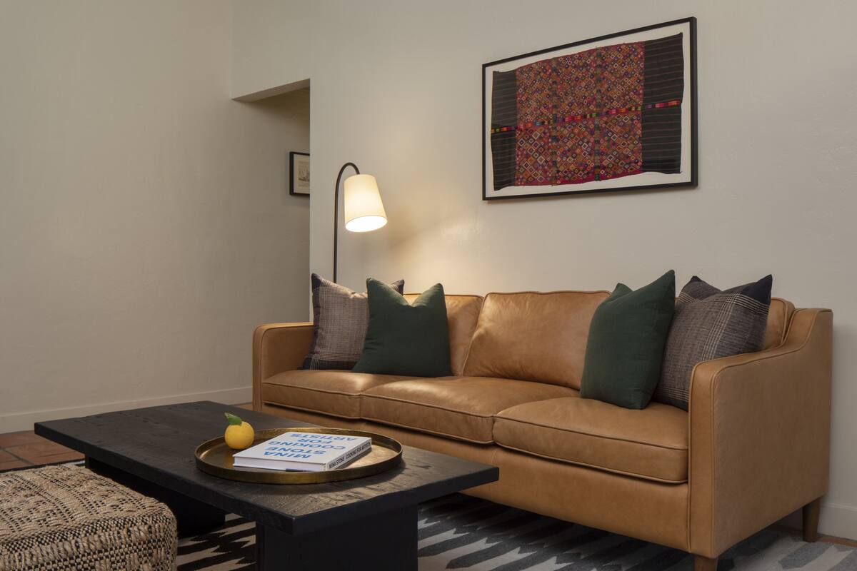 A living room with a leather sofa, a coffee table, a lamp, and a framed artwork on the wall.