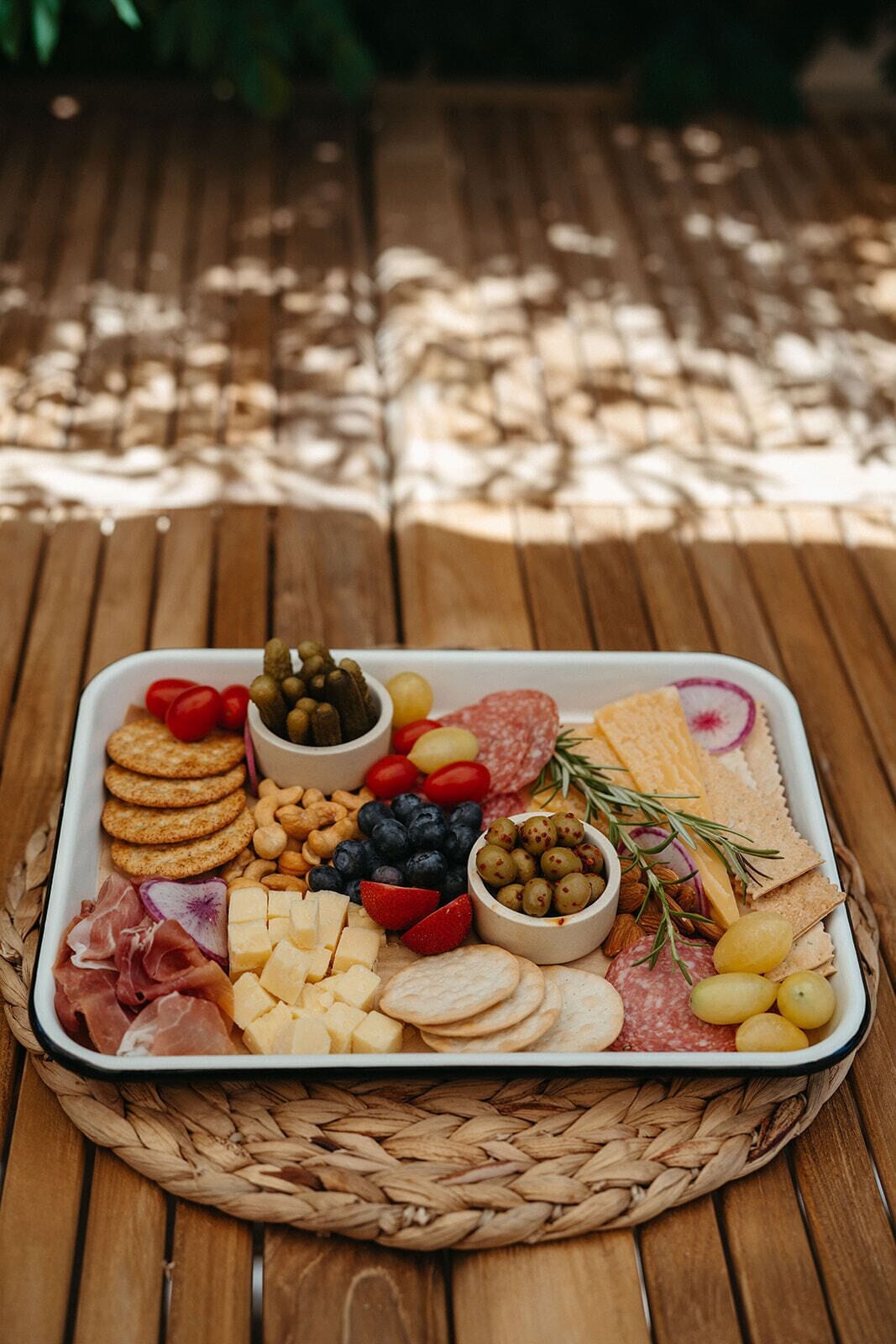 A charcuterie board with various cheeses, meats, olives, and crackers on a woven mat.