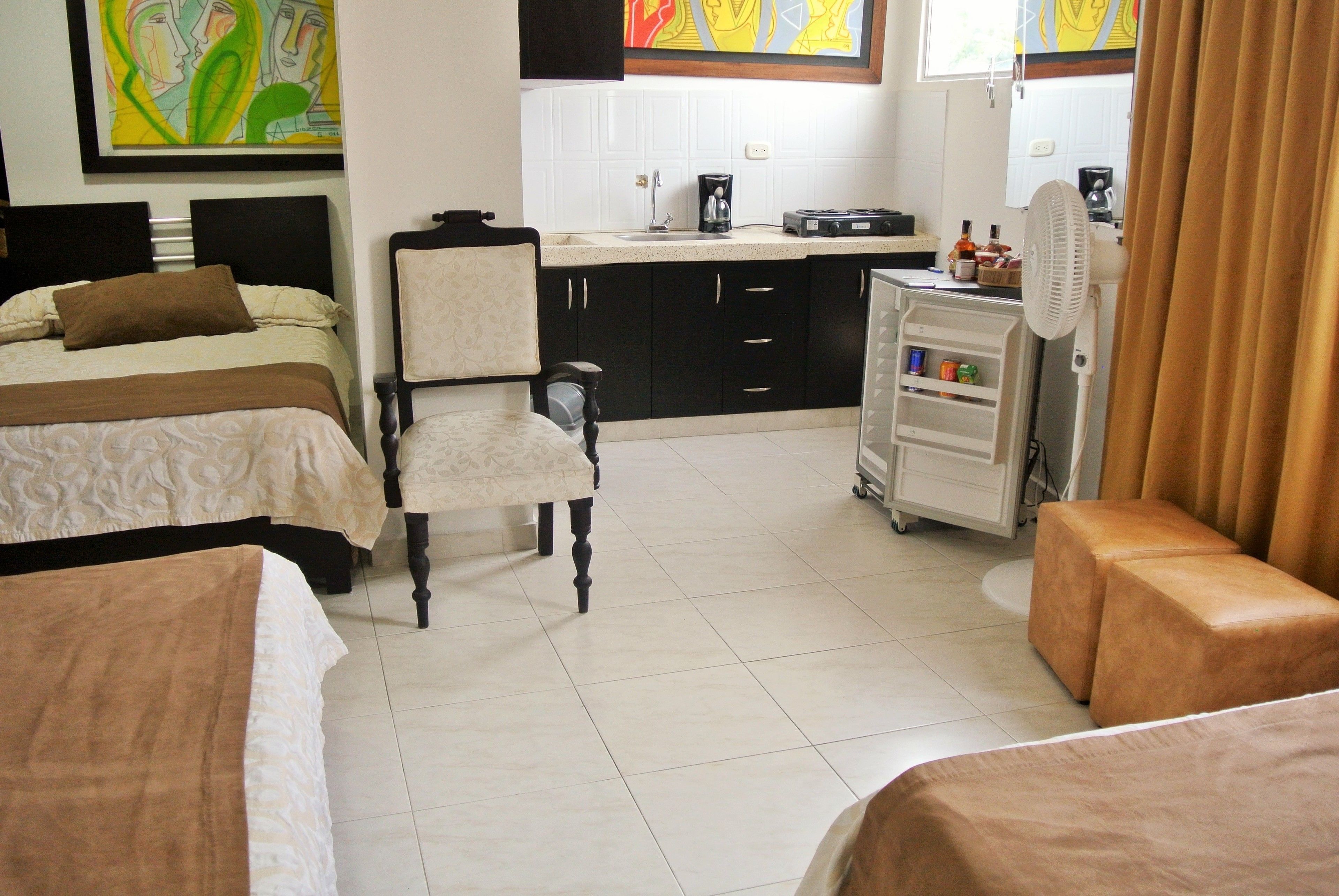 Habitación de hotel con dos camas, una kitchenette, una silla, una mesita y un ventilador.