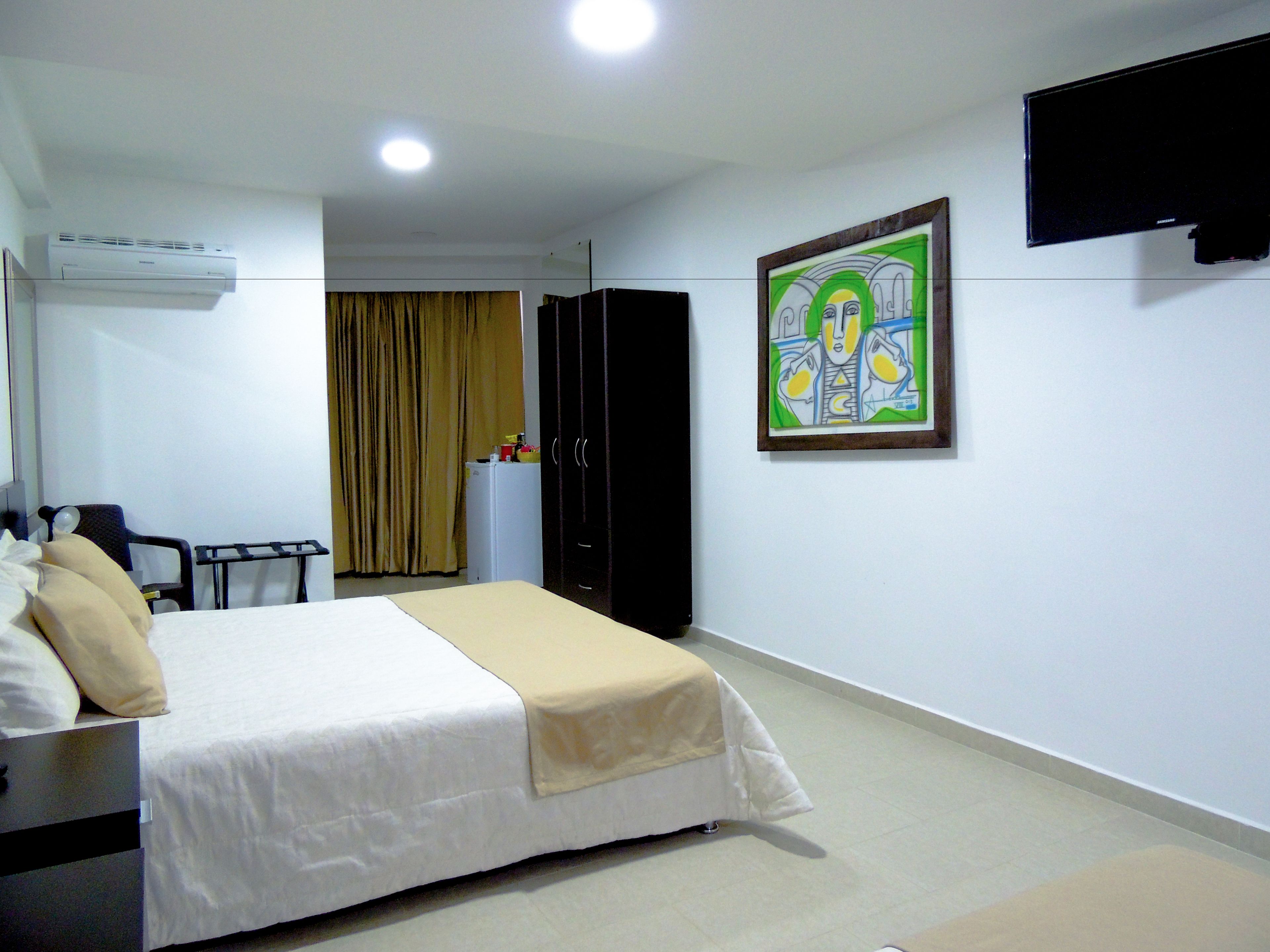 A hotel room with a bed, a desk, a wardrobe, and a painting on the wall.