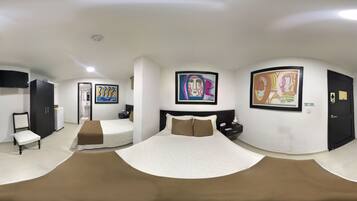 Una habitación de hotel moderna con una cama curvada, un televisor de pantalla plana, un pequeño escritorio y obras de arte en las paredes.
