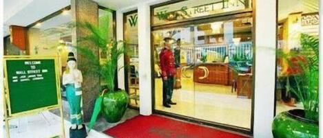 Ingresso di un hotel con tappeto rosso, cartello di benvenuto e una grande pianta in vaso.