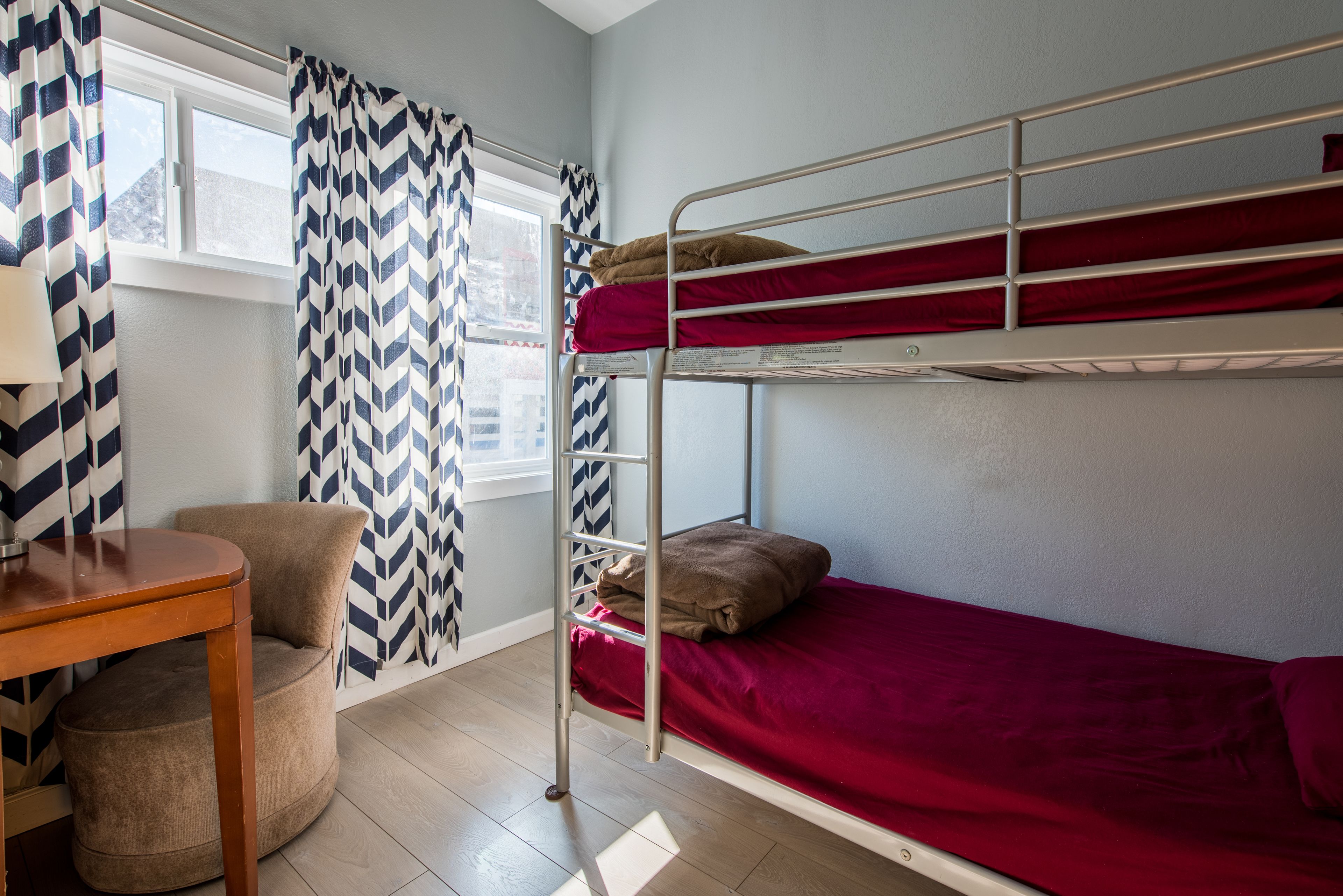 Una cama litera con ropa de cama roja, una silla de madera y una cortina estampada.