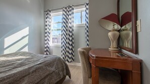 Un dormitorio con cama, una silla, una mesa y una ventana con cortinas.