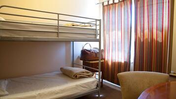 A single bed with a metal frame, a lower bunk, a small table with a chair, and a striped curtain.