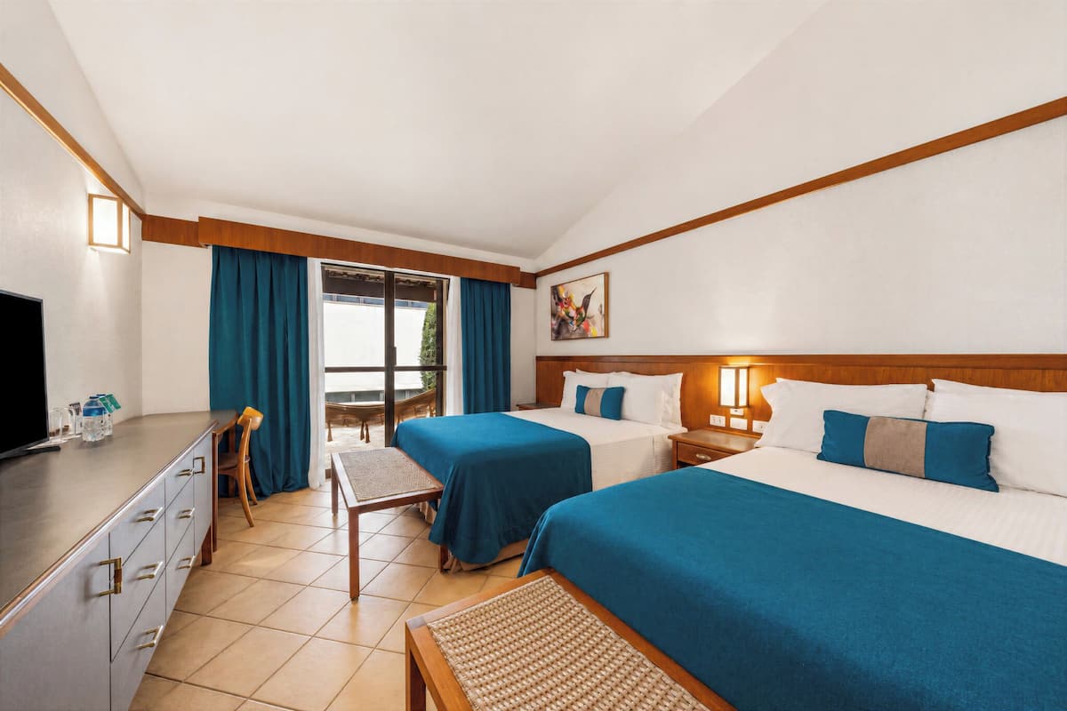 A hotel room with two beds, a desk, a TV, and a window with curtains.