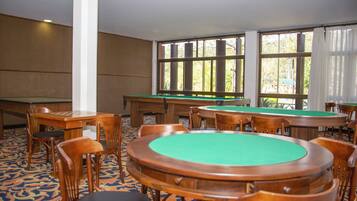 A room with multiple pool tables, chairs, and large windows with curtains.