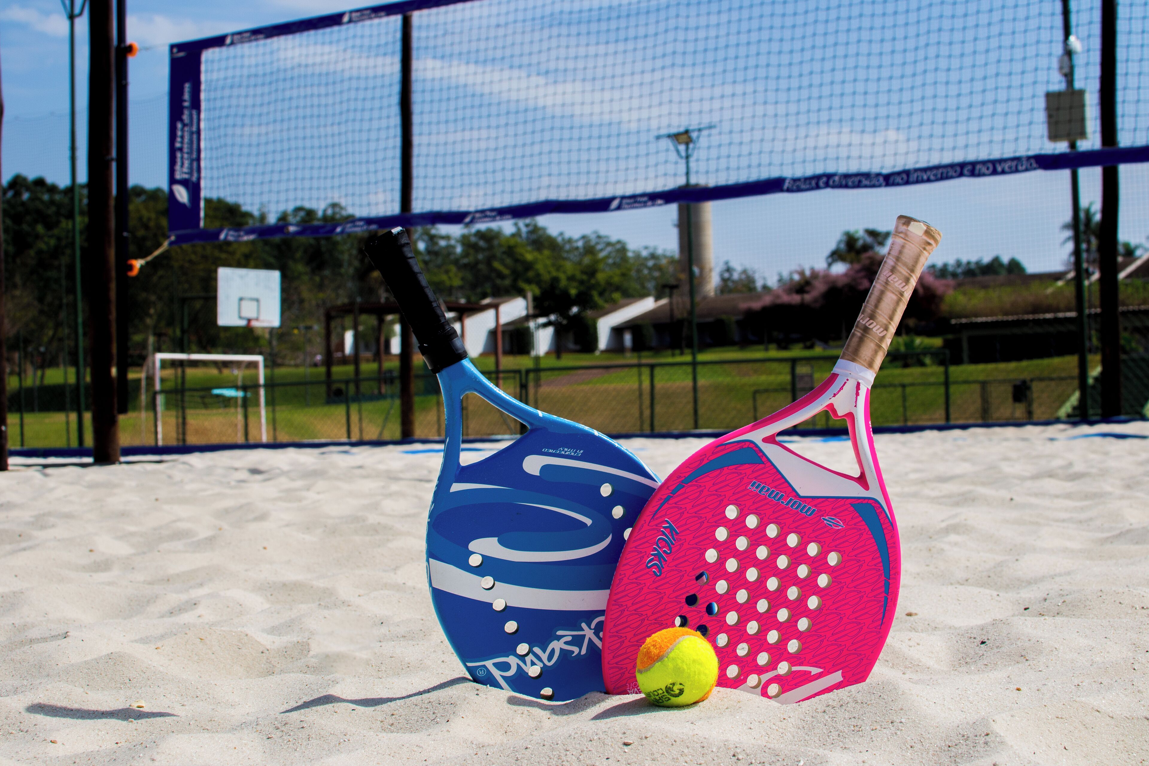 En strandvolleybollplan med ett nät, två volleybollar och två racketar.