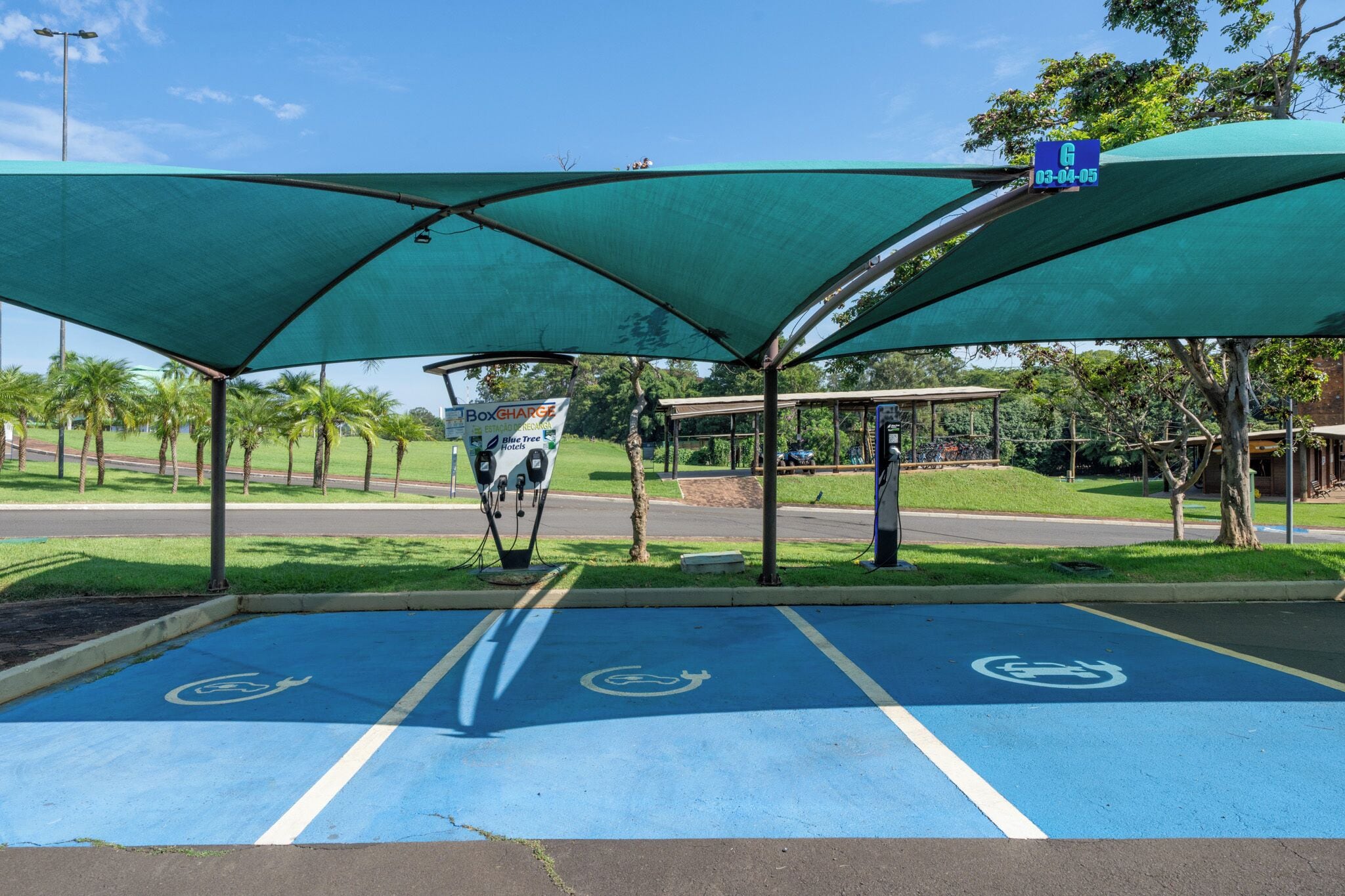 A parking area with blue handicapped parking spaces, a canopy, and a sign for Box Charge.