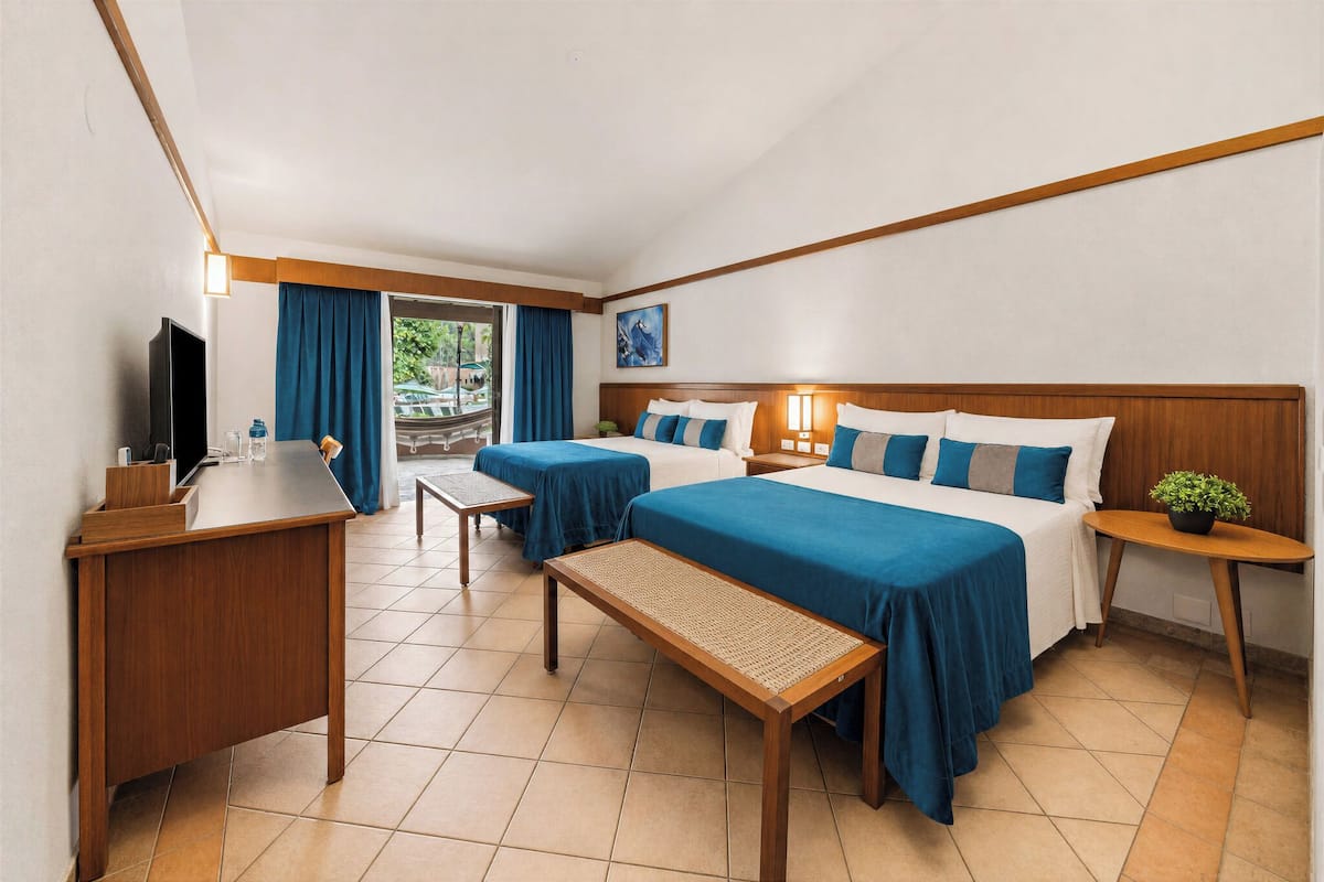 A hotel room with two beds, a desk, a television, and a view of the outdoors.