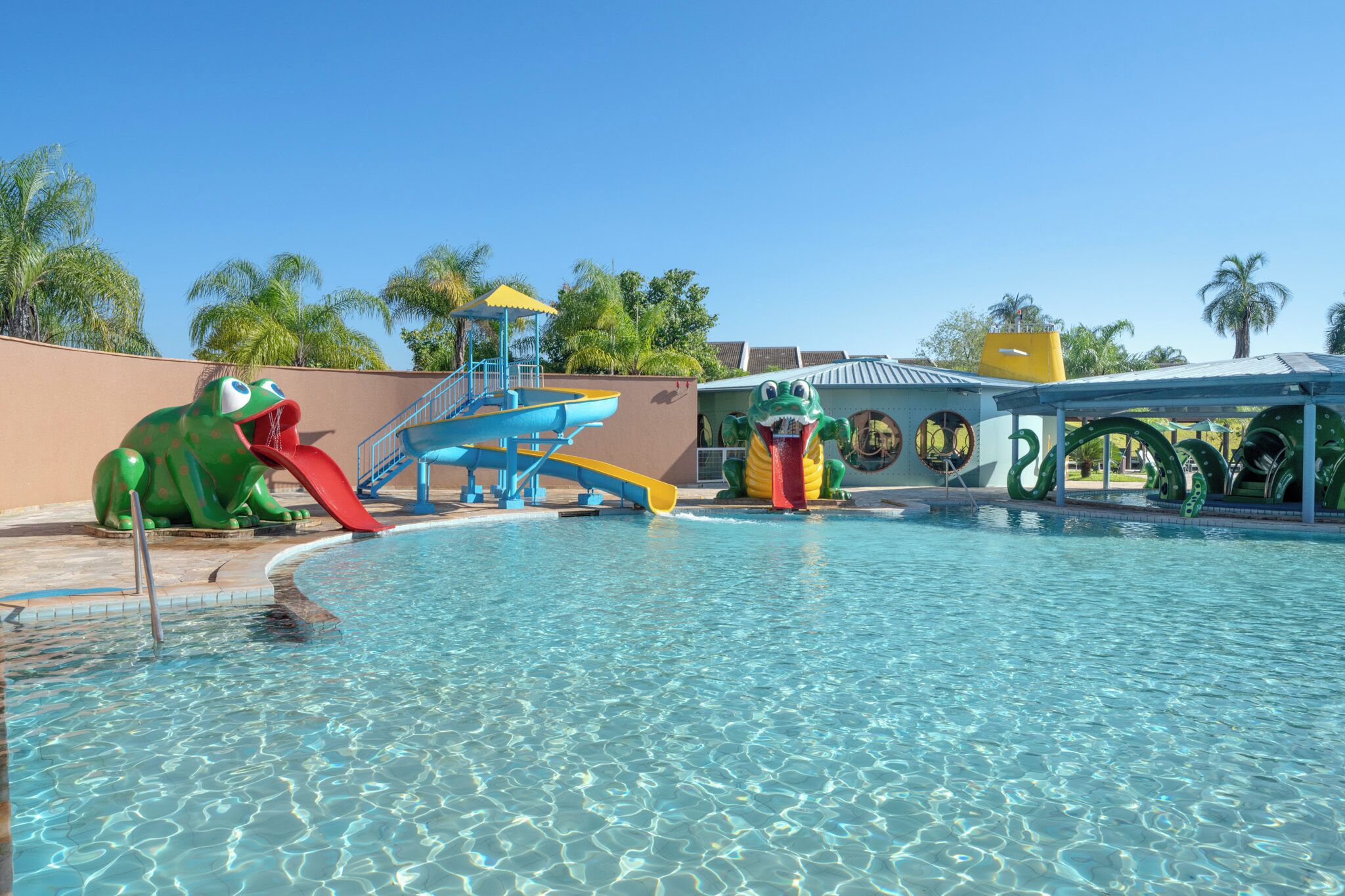 Una piscina con toboganes y una zona de juegos con temática de ranas.