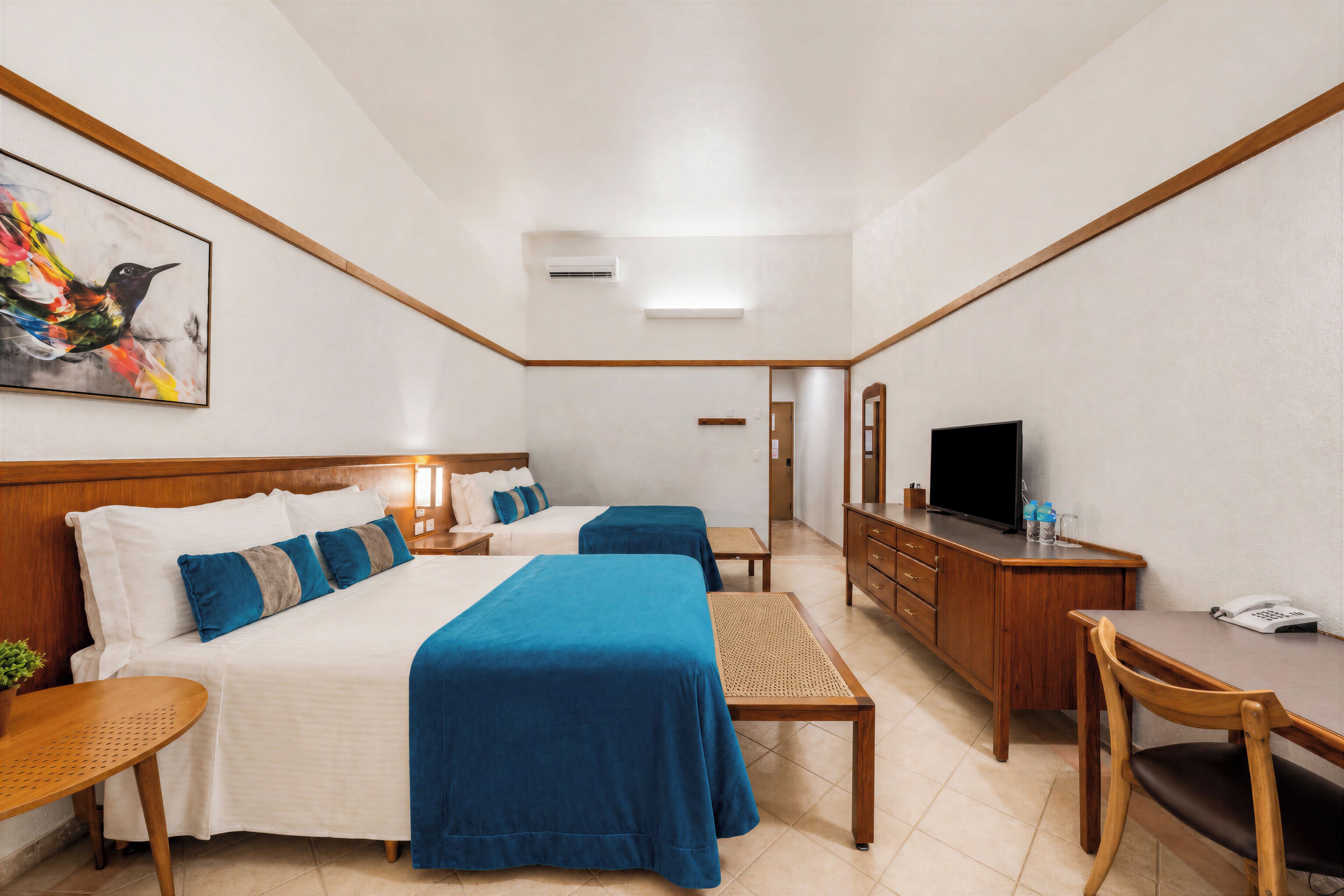Quarto de hotel com duas camas, uma escrivaninha, televisão e um quadro na parede.