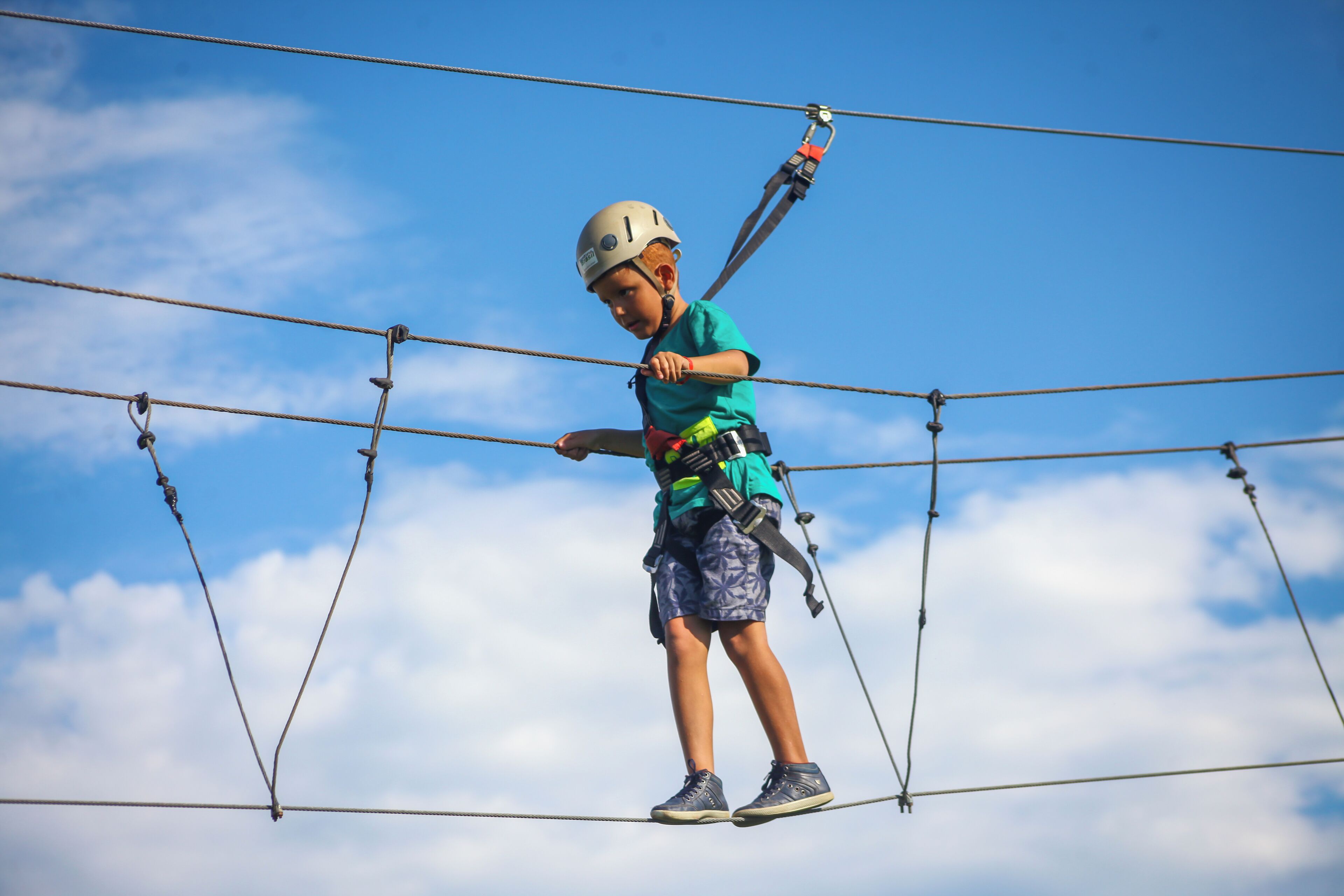 A person on a zip line with safety harness and helmet, against a clear sky.