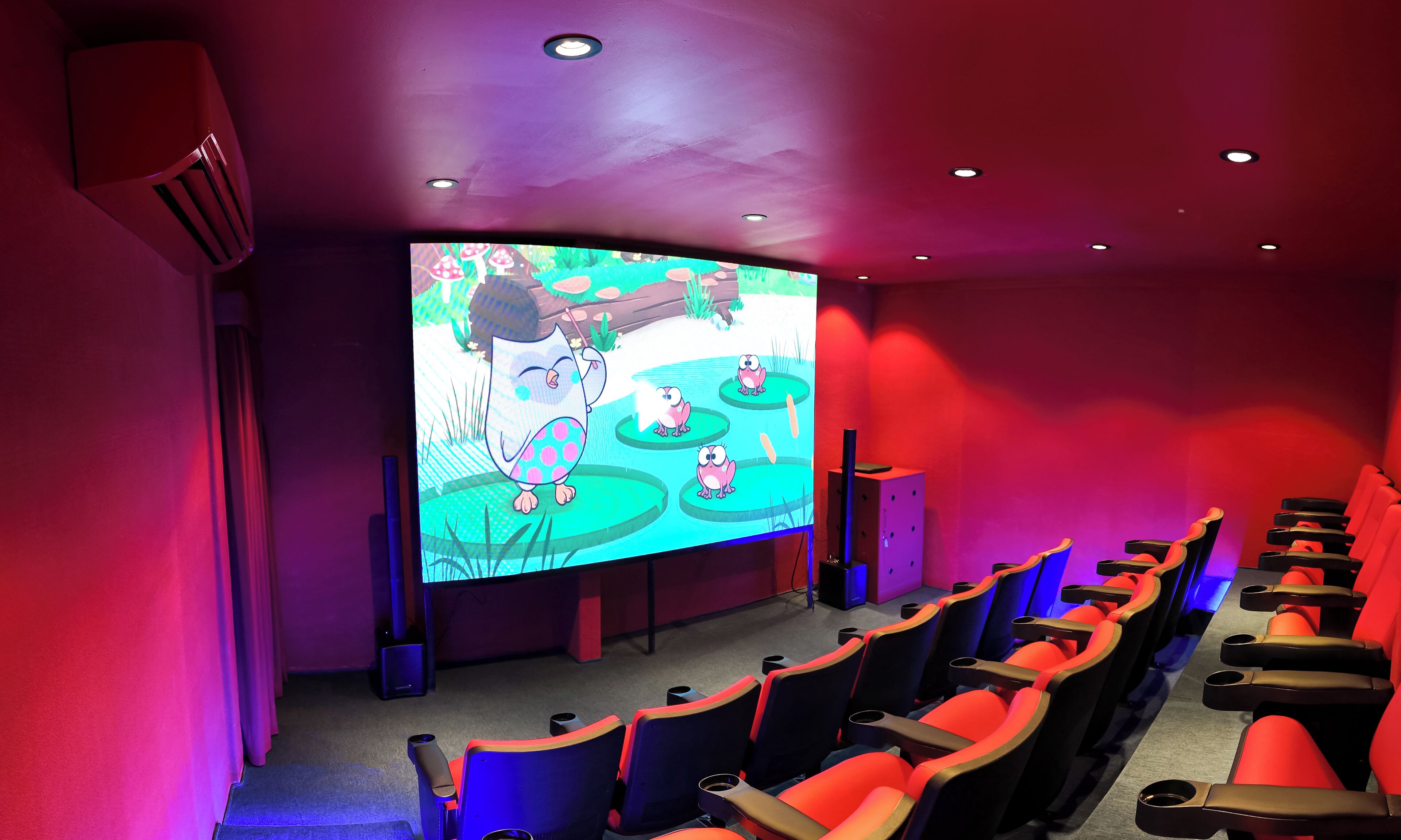 A movie theater with rows of red and black seats, a large screen, and a red ceiling.