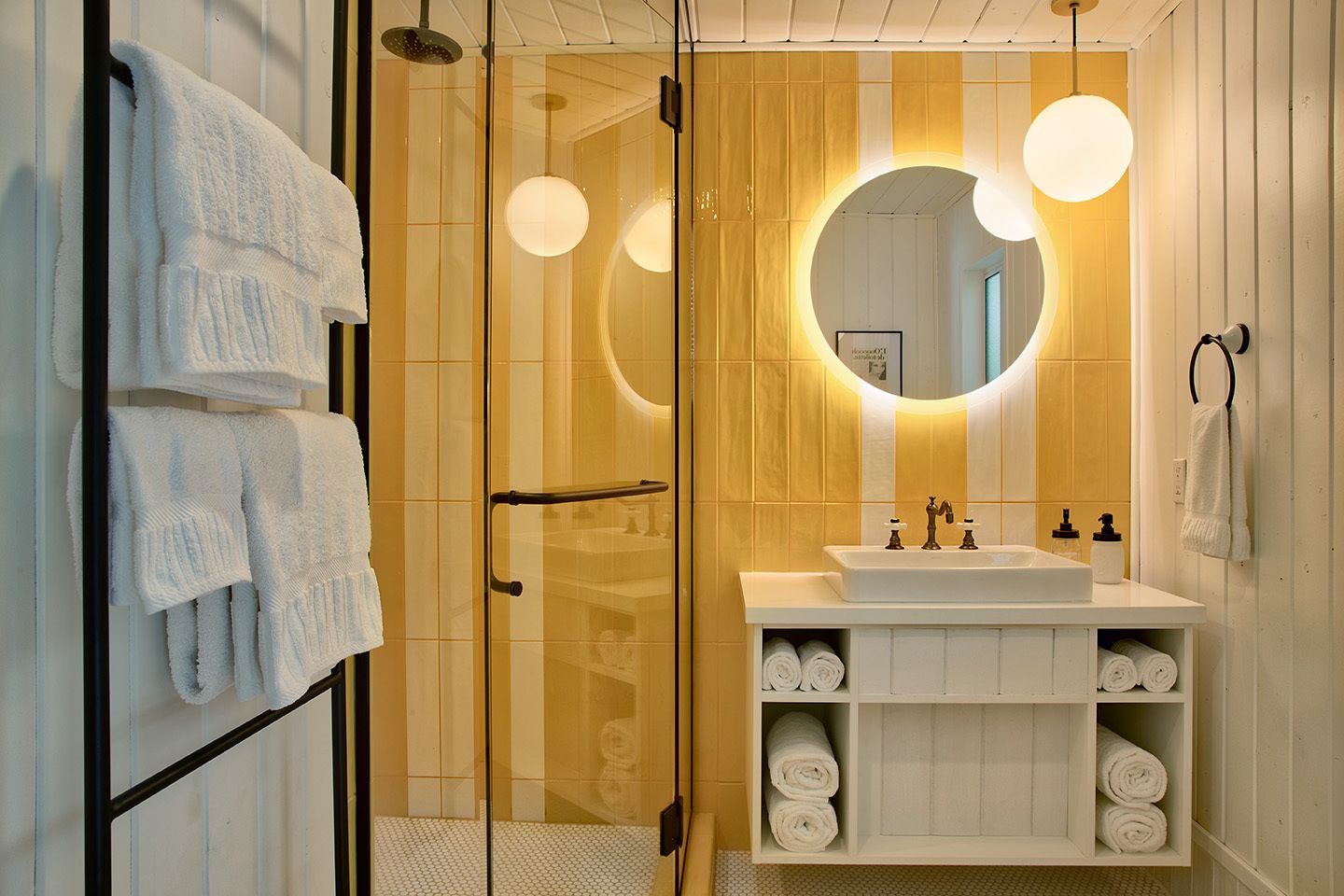 A modern bathroom with a glass shower enclosure, a white sink with a vanity, and a large mirror with circular lighting.