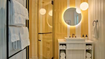 A modern bathroom with a glass shower enclosure, a white sink with a vanity, and a large mirror with circular lighting.