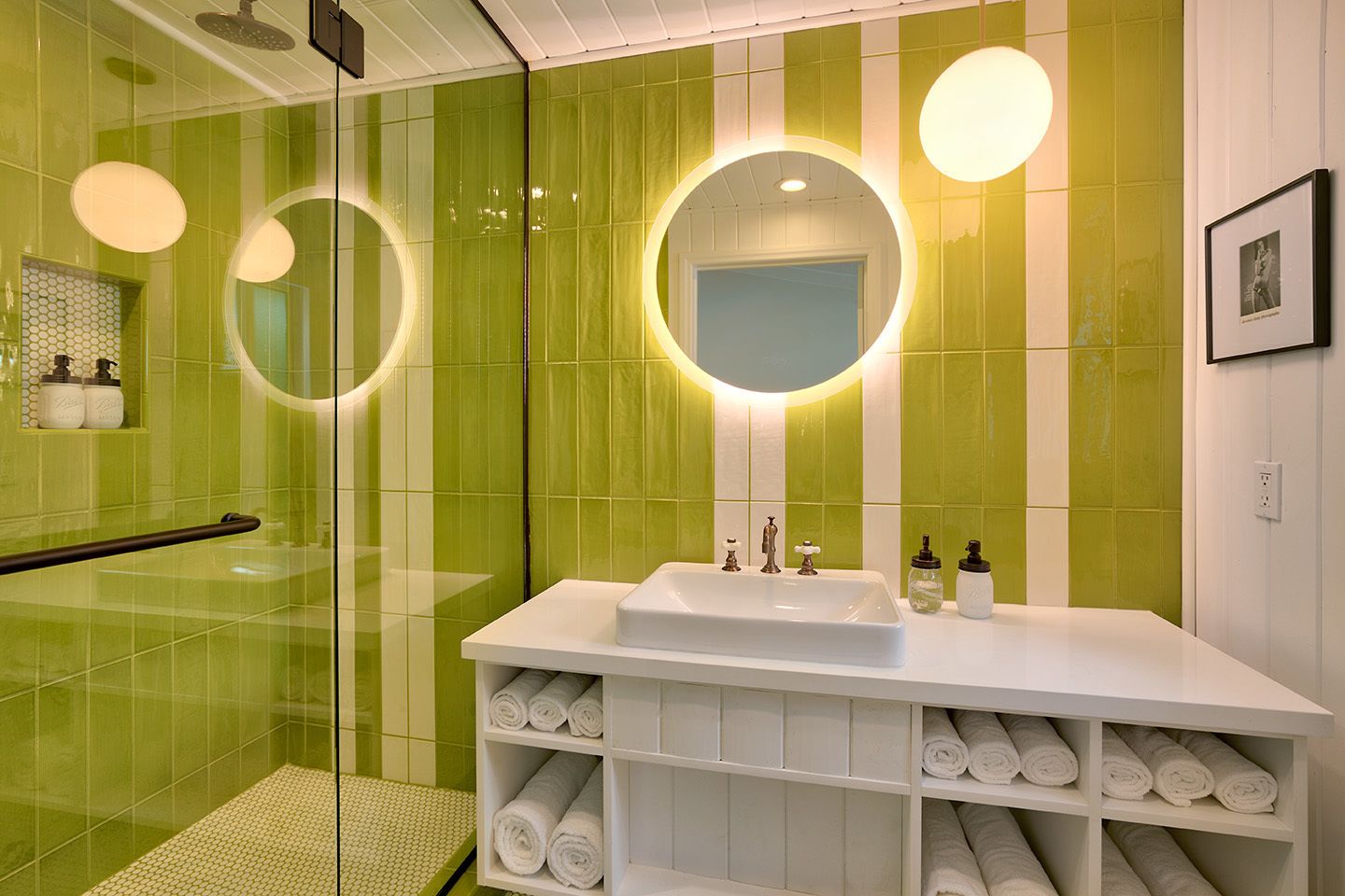 A modern bathroom with green tiles, a white sink, and a glass shower enclosure.