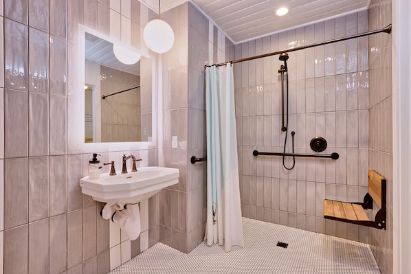 Une salle de bain moderne avec un lavabo blanc, un miroir et un espace douche agrémenté d’un banc en bois.
