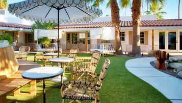An outdoor patio area with wicker furniture, a white umbrella, and a well-maintained lawn.