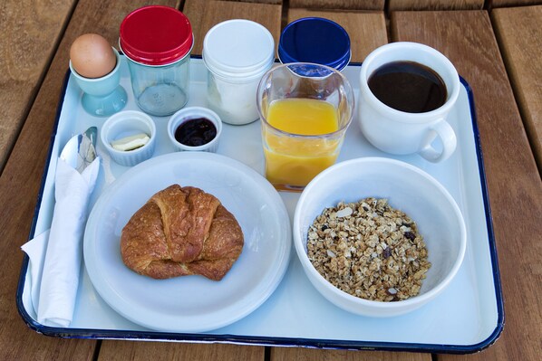 Un plateau de petit-déjeuner avec un croissant, un bol de granola, du jus d’orange, du café et un œuf à la coque.