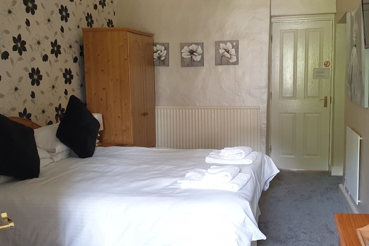 Una habitación de hotel con cama, armario, radiador, puerta y cafetera.