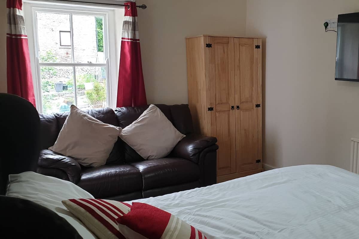 Un dormitorio con cama, sofá de cuero, armario de madera y televisión en la pared.
