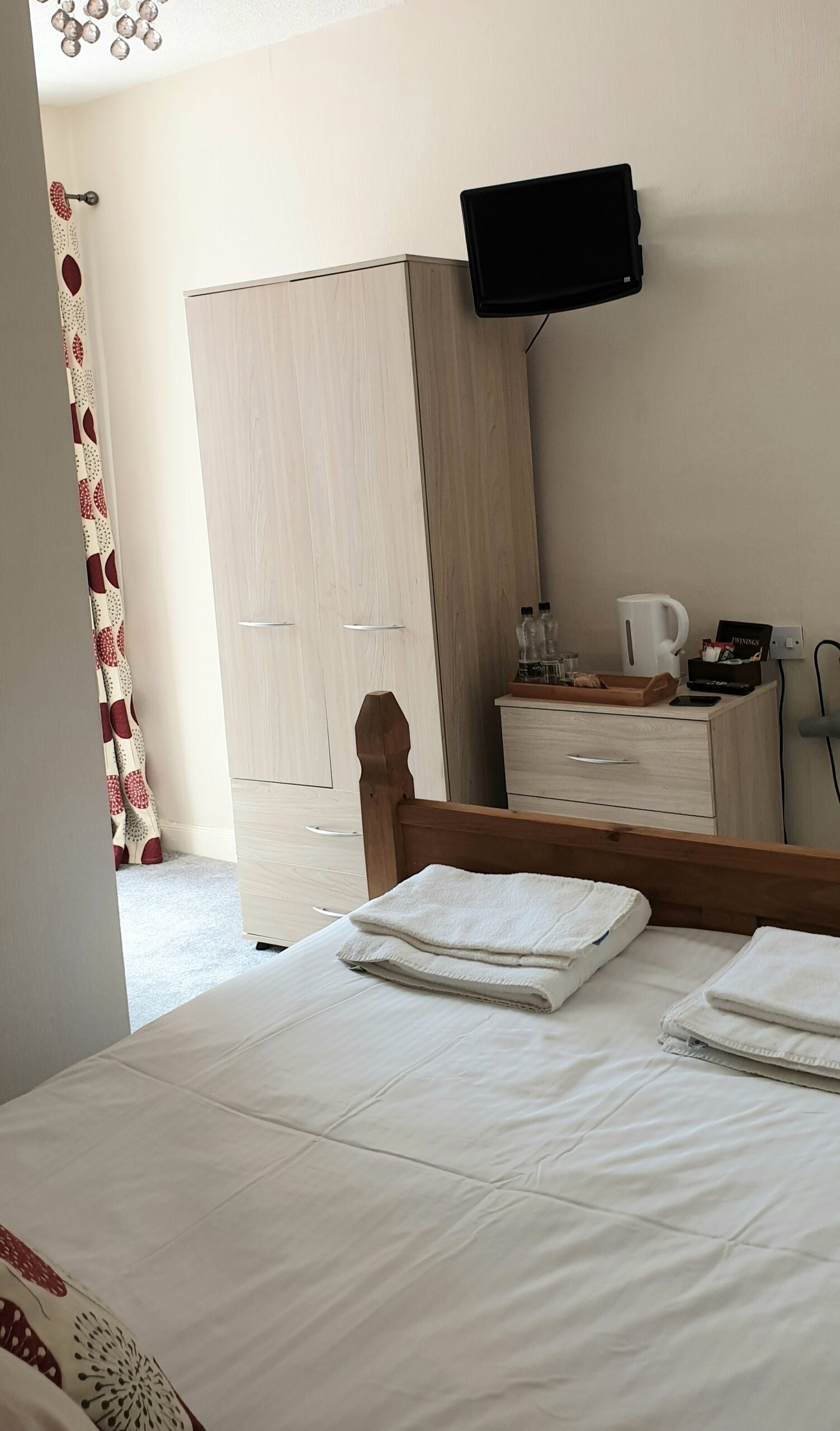 Een slaapkamer met een bed, een houten hoofdbord, een dressoir met spiegel, een aan de muur bevestigde televisie en een kledingkast.