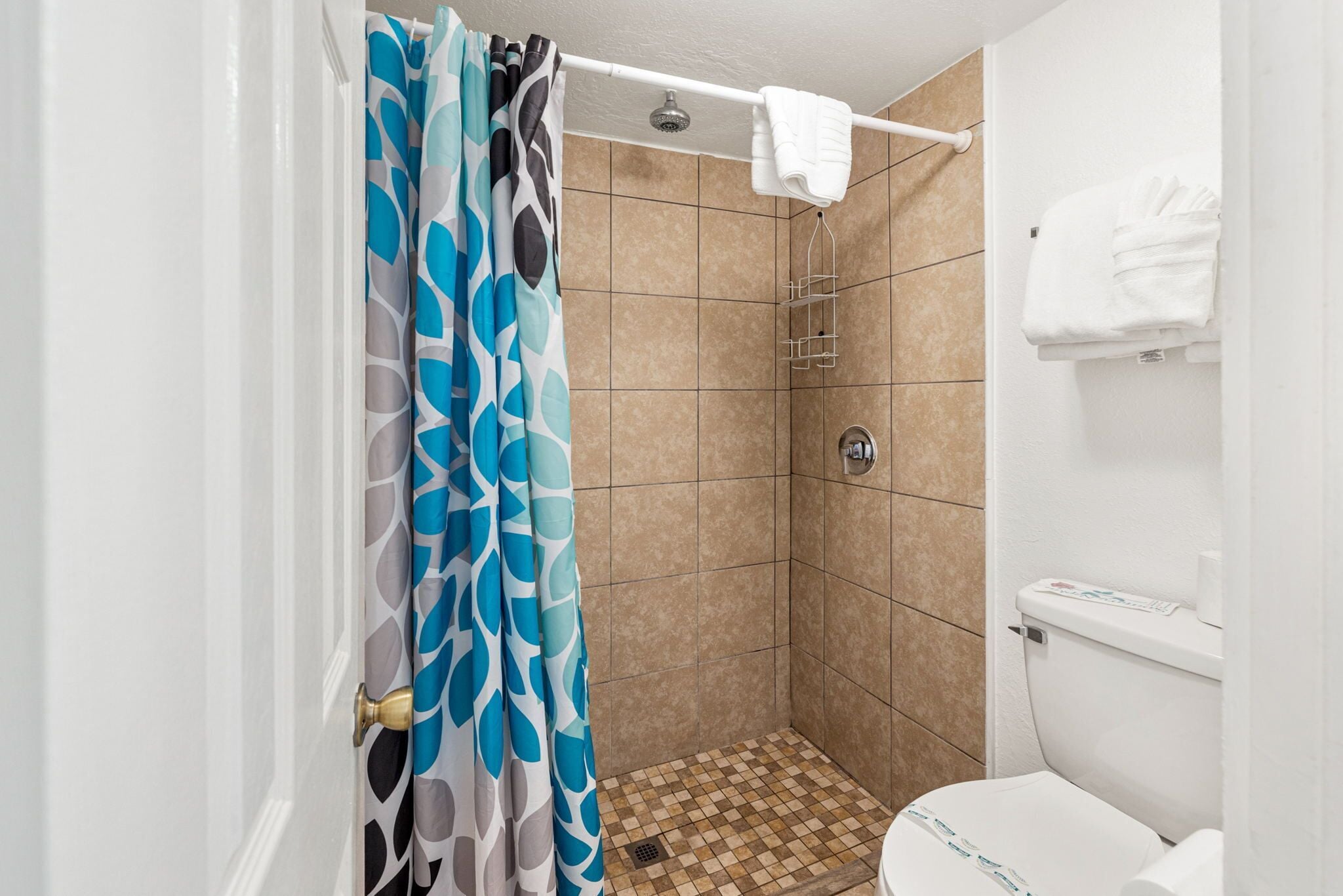 A small, tiled shower area with a shower curtain, a toilet, and a towel rack.