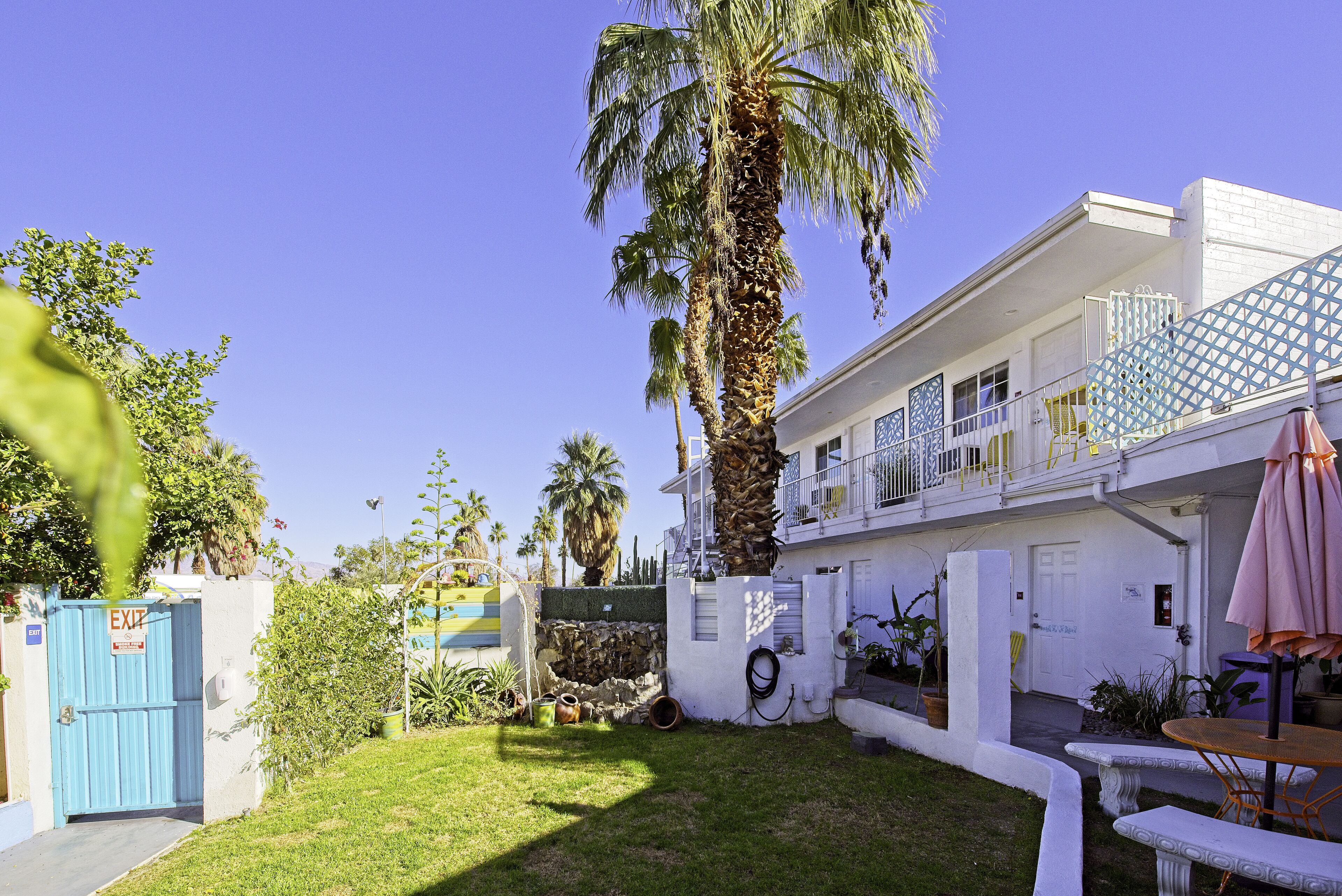A white building with a balcony, a palm tree, and a small garden.