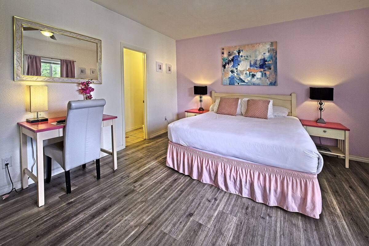 Une chambre d’hôtel avec un grand lit, un bureau avec une chaise, deux tables de chevet avec des lampes, un miroir et un tableau au mur.