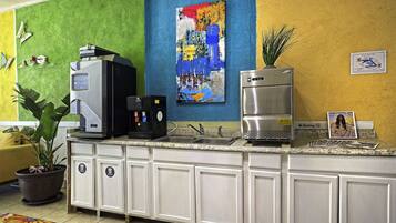 A kitchen with a coffee machine, a sink, and a refrigerator. There is a plant on the counter and a painting on the wall.