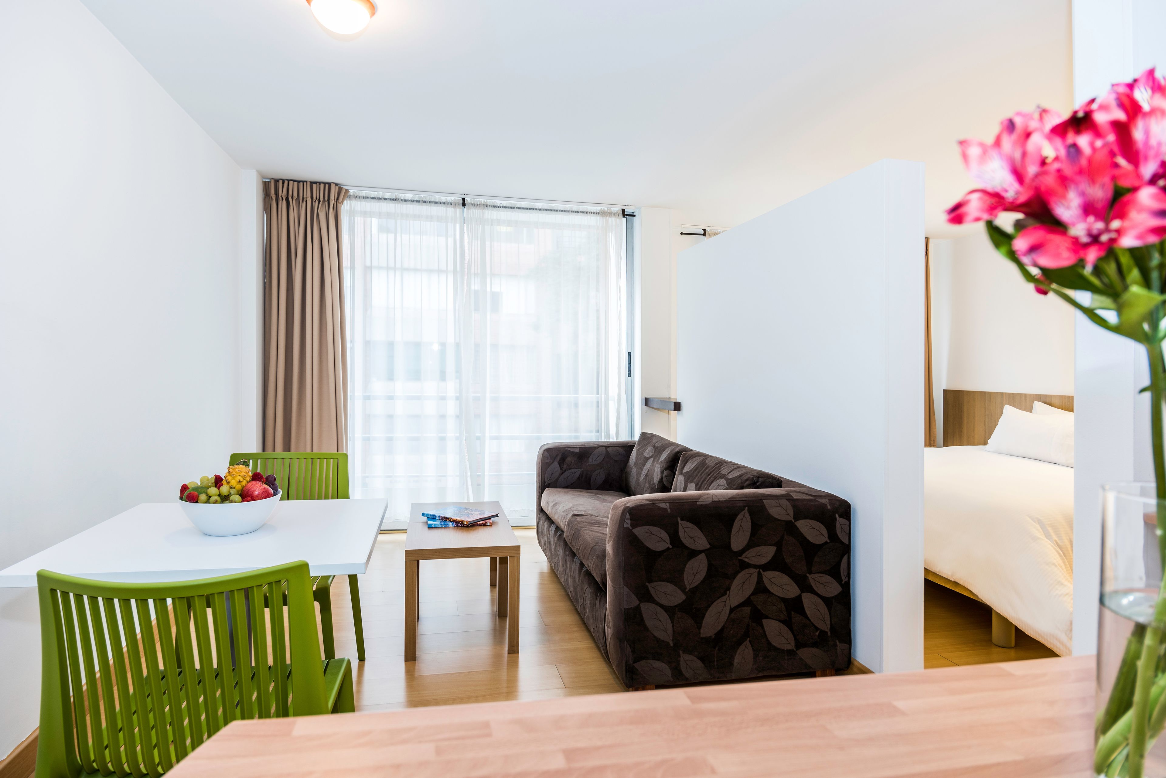 A modern room with a dining table, green chairs, a sofa, and a bed.