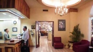 A hotel lobby with a reception desk, a chandelier, a red armchair, and a potted plant. - Hotel 5a Avenida (Monterrey)