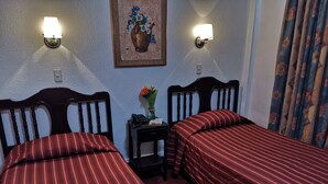 A room with two beds, each with striped bedding, a small bedside table with a phone and a vase of flowers, and wall-mounted lights. - Hotel 5a Avenida (Monterrey)