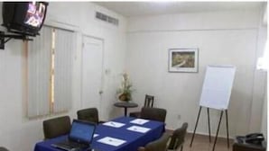 A conference room with a long table, chairs, a laptop, papers, a whiteboard, and a television. - Hotel 5a Avenida (Monterrey)