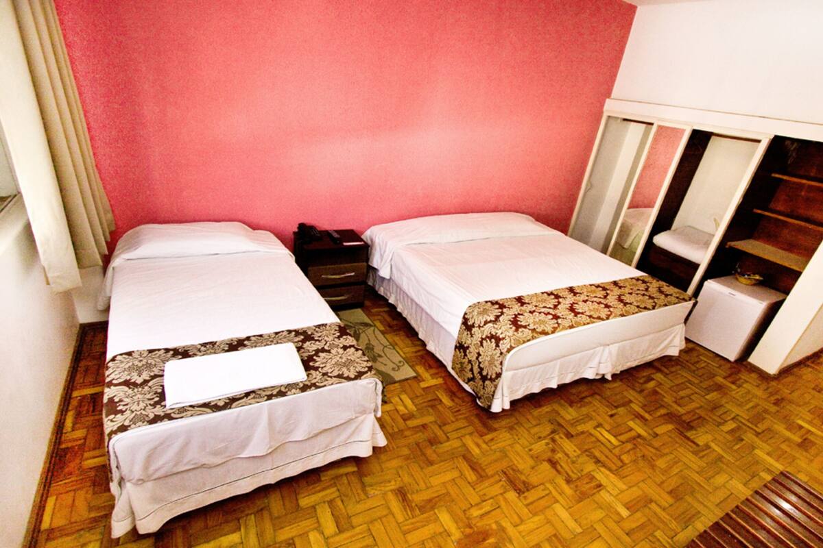 Ett litet hotellrum med två enkelsängar, ett trägolv, en röd vägg, ett litet skrivbord och en garderob.