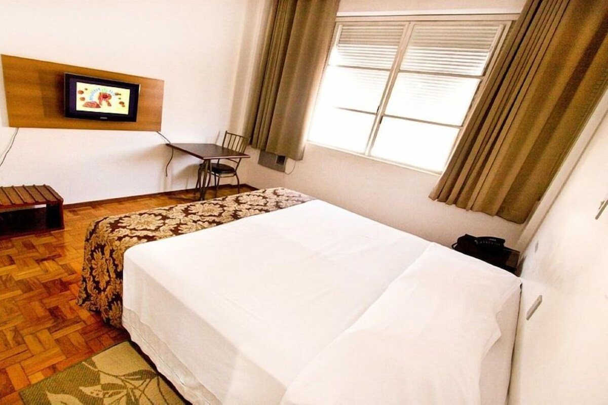 Ein Hotelzimmer mit einem Bett, einem Schreibtisch, einem Sessel und einem Fernseher an der Wand.