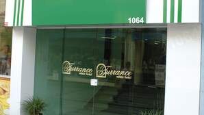 Entrada de un hotel con fachada verde y blanca, donde se destaca el nombre 'Turrance White Hotel', y dos macetas con plantas a la entrada.