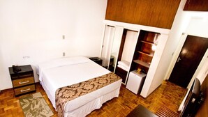 Habitación de hotel con cama, un escritorio pequeño, armario y refrigerador.