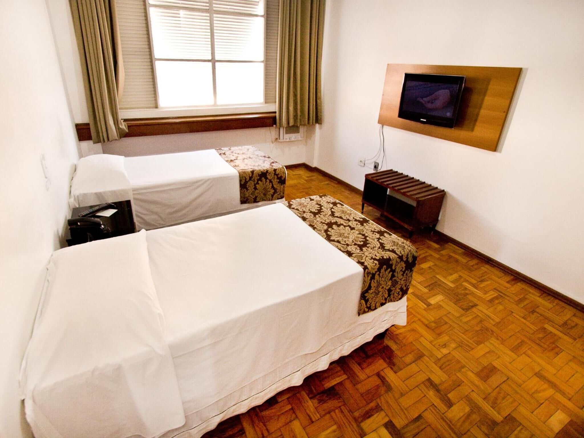 A hotel room with two beds, a TV mounted on the wall, and a window with curtains.