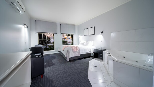 Quarto de hotel moderno com cama, escrivaninha, cadeira, banheira e janela com persianas.
