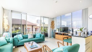 A spacious living room with a large sofa set, a coffee table, and a kitchen area with a TV. - AQ-VA Hotel & Villas Seminyak (Legian)