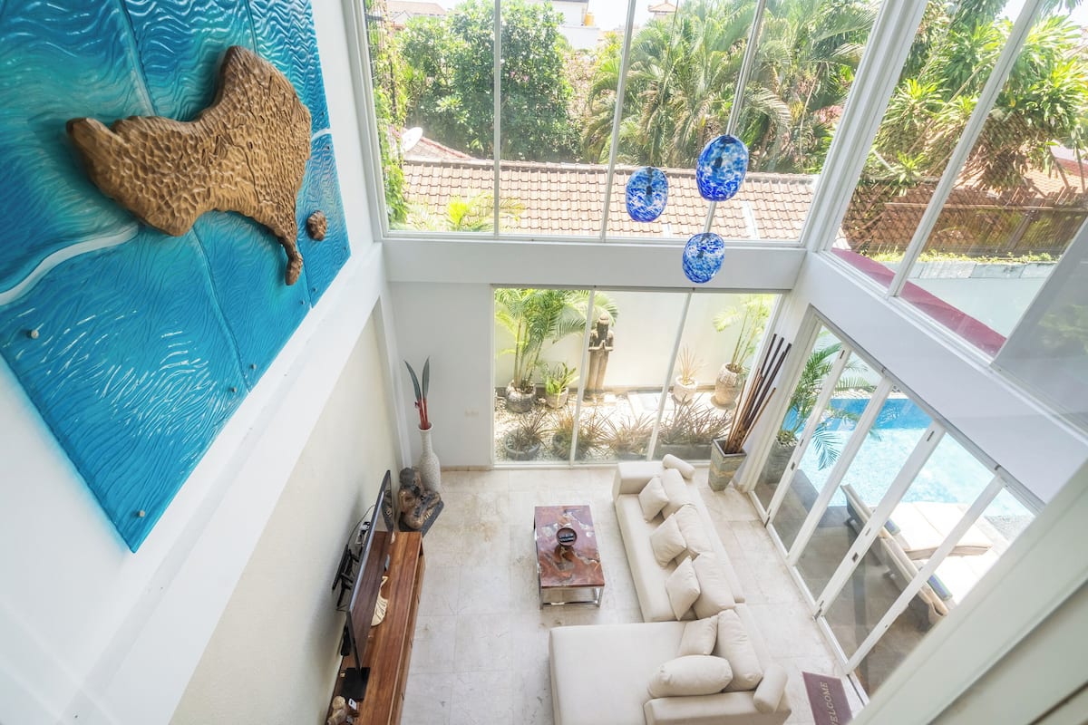 Ein großzügiger Wohnbereich mit einem großen Fenster zum Schwimmbad, einer Wanddekoration und einem Sofa.