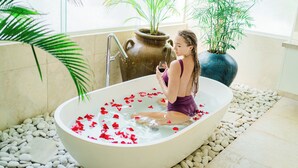 A woman in a bathtub filled with water and rose petals, surrounded by potted plants and a stone pathway. - AQ-VA Hotel & Villas Seminyak (Legian)