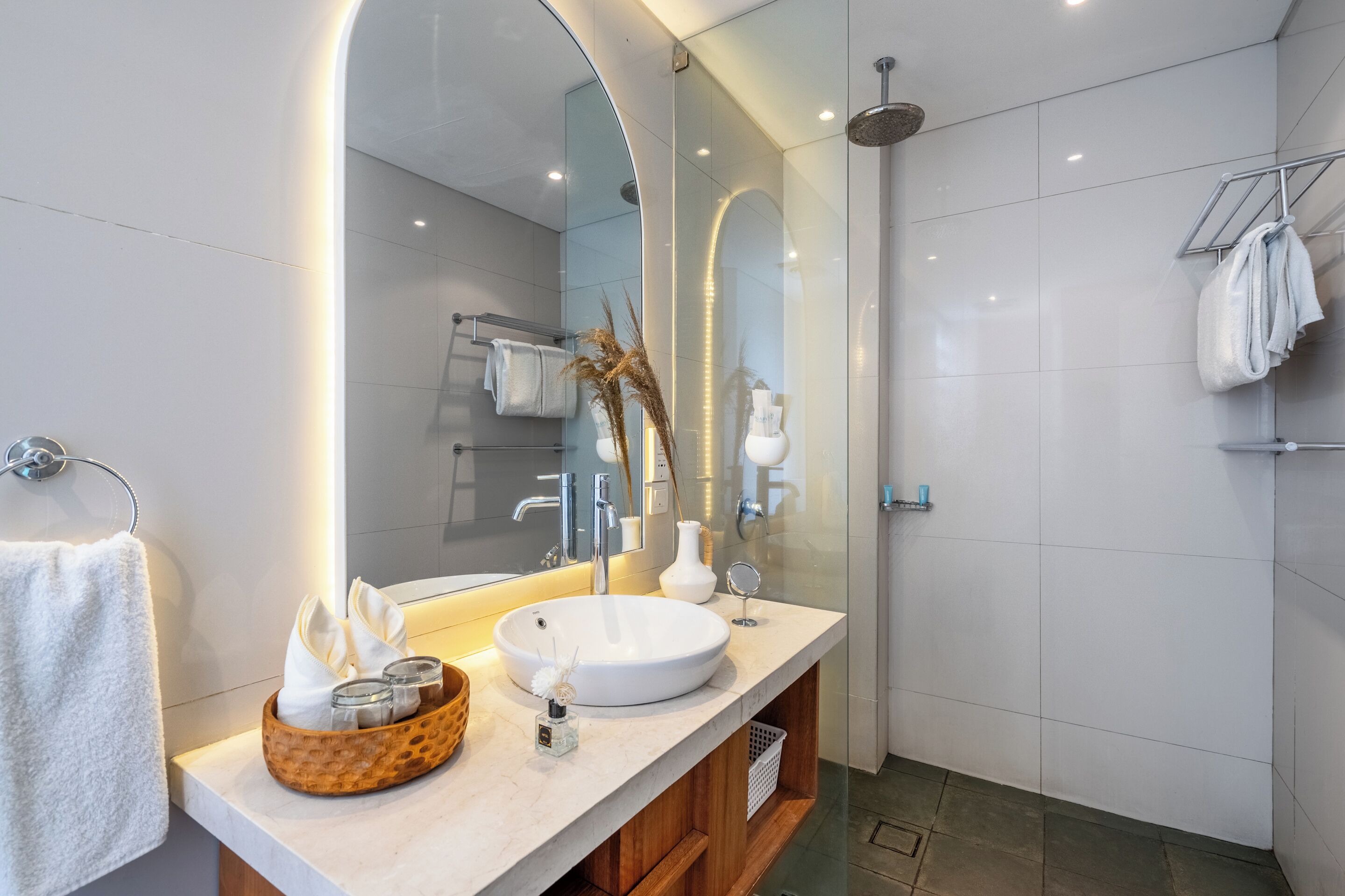 A modern bathroom with a large mirror, a round sink, and a shower area.
