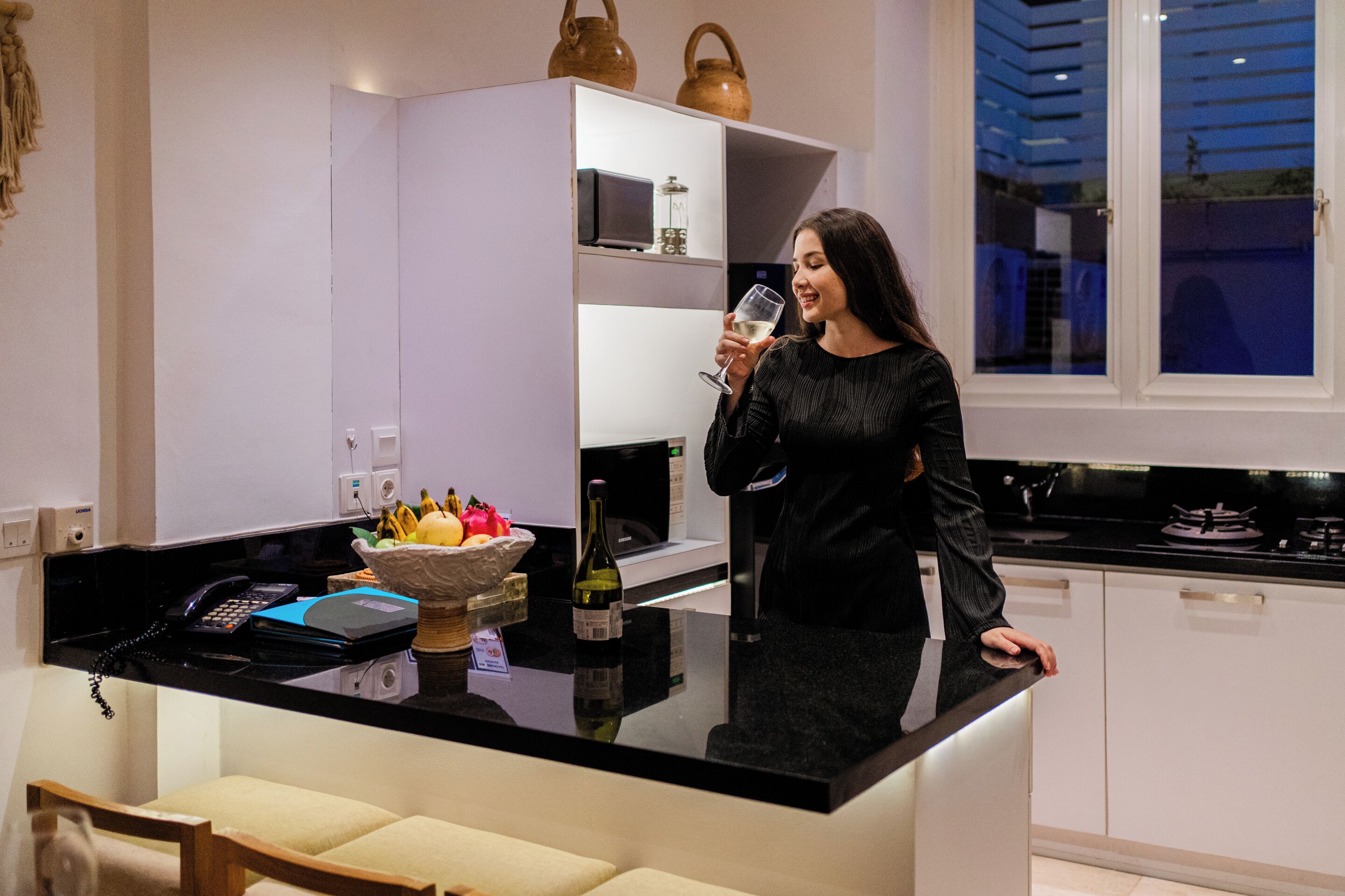 A modern kitchen with a black countertop, white cabinets, and a window with a view of the outside.