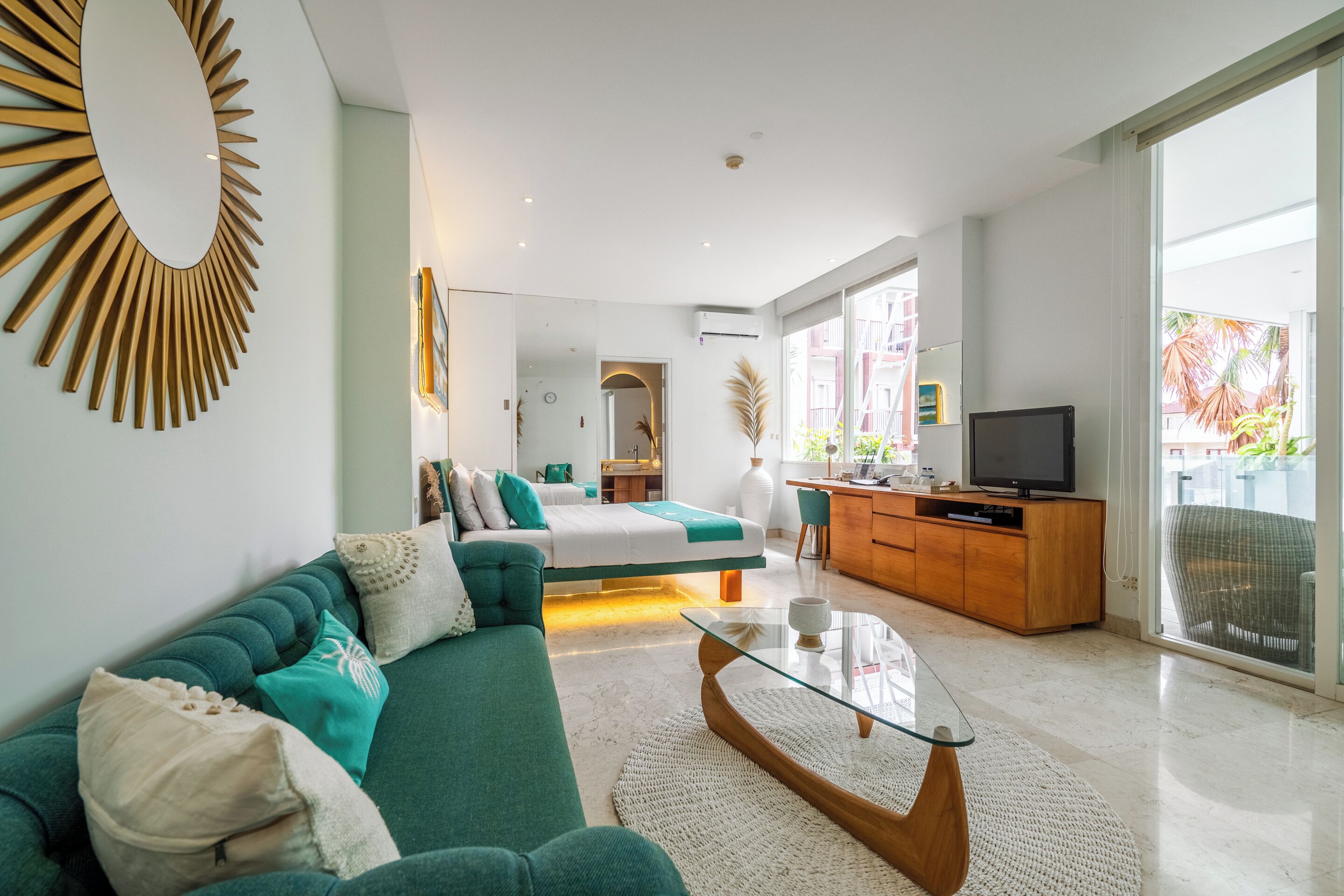 A modern living room with a sofa, a glass coffee table, a TV, and a view of the outdoors.