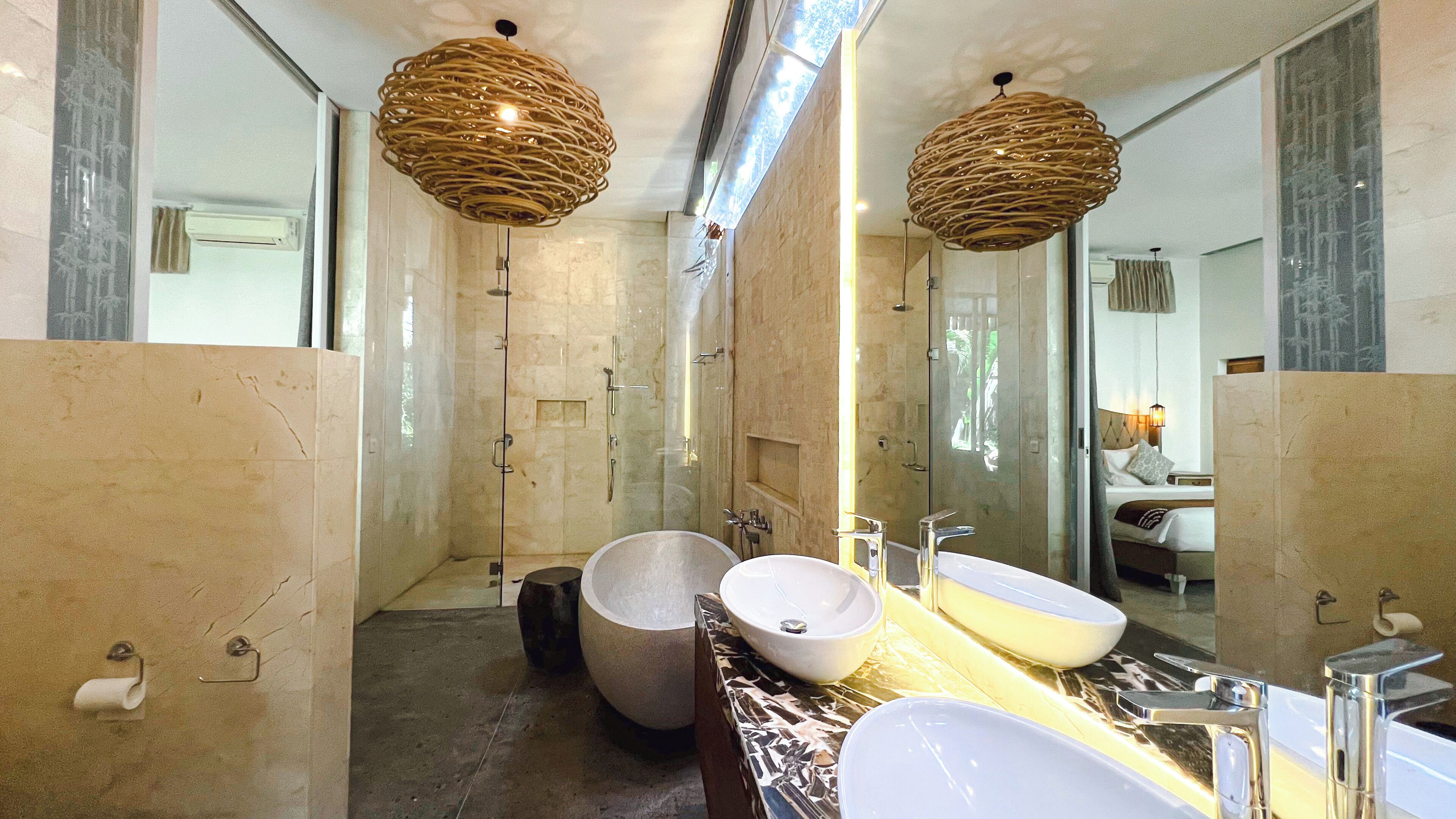 A modern bathroom with a large mirror, two sinks, a bathtub, and a shower.