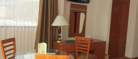 Una habitación de hotel con una mesa de comedor, sillas, televisor, escritorio y armario.